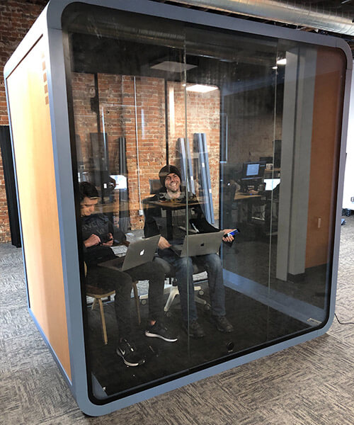 Two people working happily in the large khaki office privacy pod